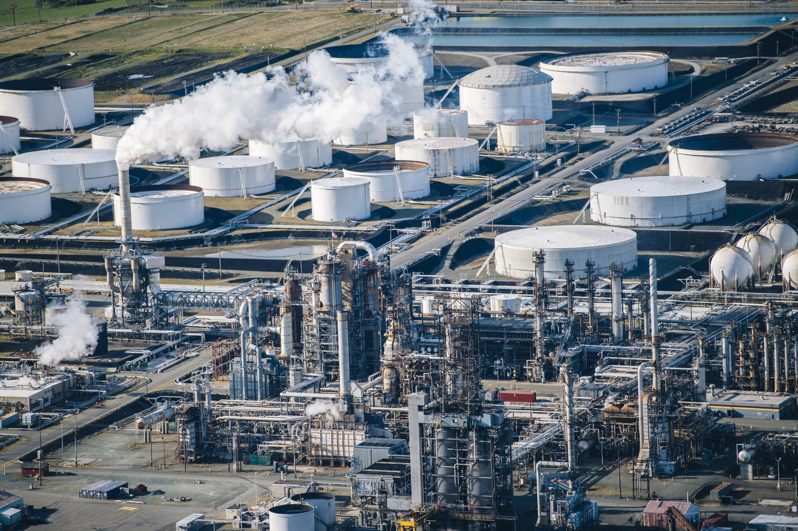 Rows of white oil storage tanks and smoke stack in oil refinery